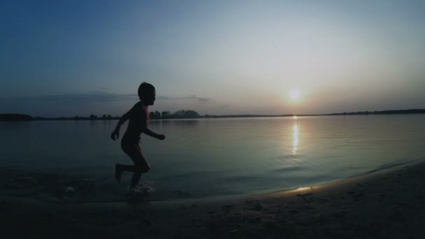 Happy Boy court le long de la plage au coucher du soleil. Mouvement lent — Video