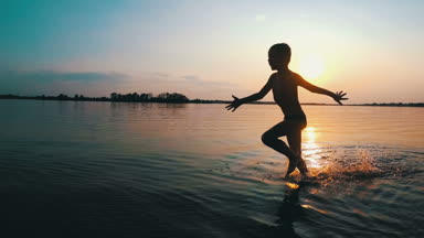 Mutlu çocuk gün batımında kumsal boyunca çalışır. Ağır çekim