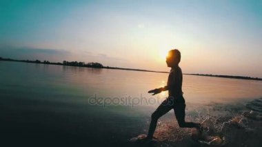 Mutlu çocuk gün batımında kumsal boyunca çalışır. Ağır çekim