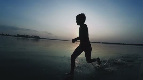 Happy Boy corre ao longo da praia ao pôr do sol. Movimento lento — Vídeo de Stock