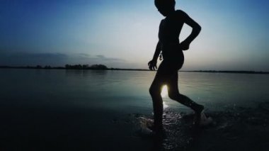 Gün batımında kumsal boyunca çalışan mutlu çocuk silüeti. Ağır çekim