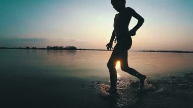 Mutlu çocuk gün batımında kumsal boyunca çalışır. Ağır çekim