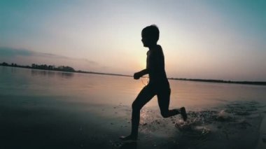 Mutlu çocuk gün batımında kumsal boyunca çalışır. Ağır çekim