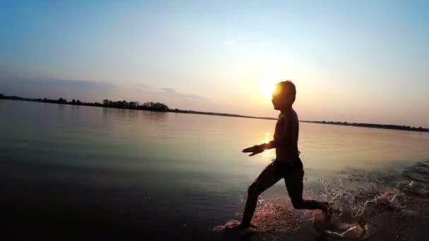 Boldog fiú fut a tengerparton naplementekor. Lassú mozgás — Stock videók