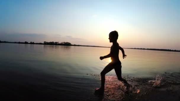Ευτυχισμένο αγόρι τρέχει κατά μήκος της παραλίας στο ηλιοβασίλεμα. Αργή κίνηση — Αρχείο Βίντεο