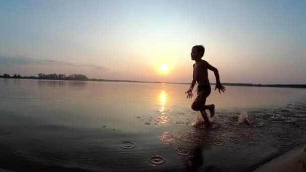 Szczęśliwe dziecko biega po plaży o zachodzie słońca. Zwolnionym tempie — Wideo stockowe