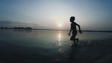 Mutlu çocuk gün batımında kumsal boyunca çalışır. Ağır çekim