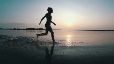 Mutlu çocuk gün batımında kumsal boyunca çalışır. Ağır çekim