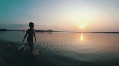 Mutlu çocuk gün batımında kumsal boyunca çalışır. Ağır çekim