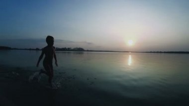 Mutlu çocuk gün batımında kumsal boyunca çalışır. Ağır çekim