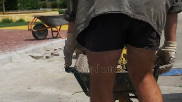 Trabajador de la construcción está conduciendo una carretilla con adoquines en un sitio de construcción — Vídeo de stock