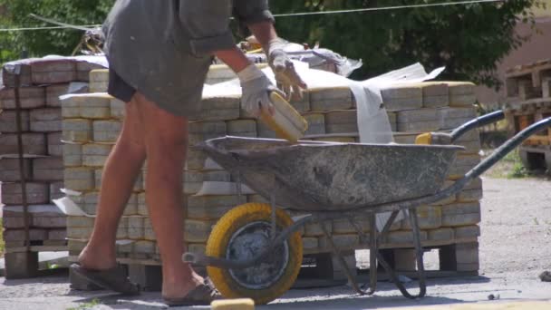 Рабочий загружает цветной тротуарный камень в тачку — стоковое видео
