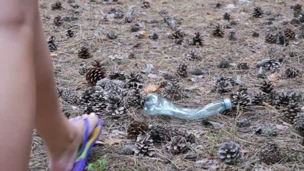 Пластикова пляшка в сосновому лісі. Жінка кусає пластикову пляшку з ногою. Повільний рух — стокове відео