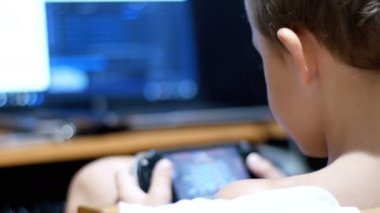 Çocuk bir taşınabilir oyun konsolu defada bir sandalyede evde oynuyor