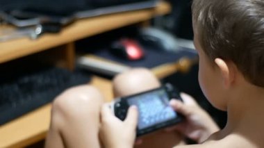 Çocuk bir taşınabilir oyun konsolu defada bir sandalyede evde oynuyor