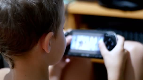 Bambino sta giocando in una console di gioco portatile seduto su una sedia a casa — Video Stock