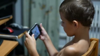 8 yaşındaki eski çocuk Video oyunları oynarken bir sandalyede evde oturan bir taşınabilir oyun konsolu üzerinde