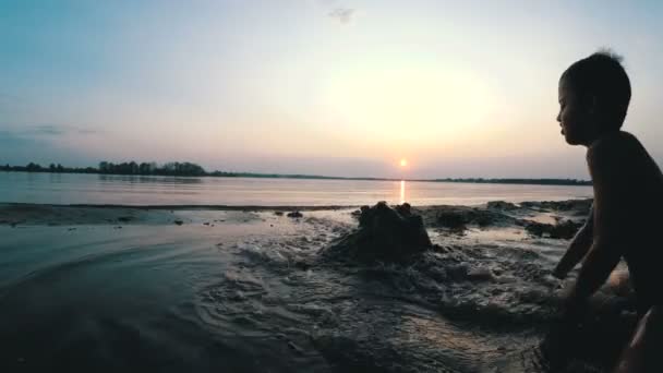 Sylwetka dziecka na plaży budynek zamek z piasku o zachodzie słońca — Wideo stockowe