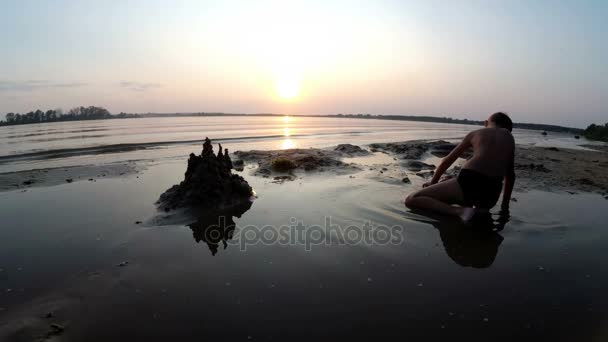 Silhouet jongetje bouwt een kasteel zand bij zonsondergang — Stockvideo