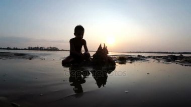 Sahilde günbatımı kum kale inşa bir çocuk silüeti