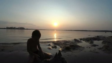 Sahilde günbatımı kum kale inşa bir çocuk silüeti