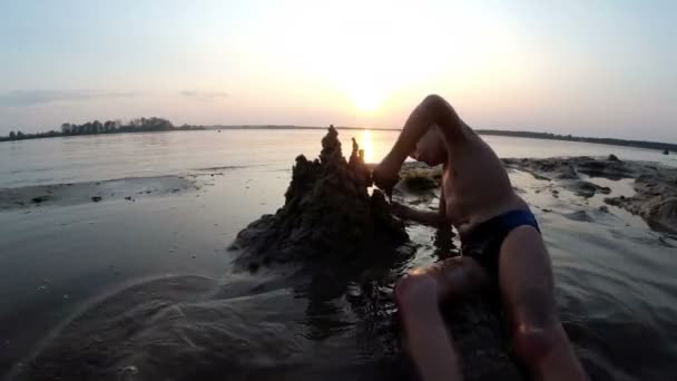 Sylwetka dziecka na plaży budynek zamek z piasku o zachodzie słońca — Wideo stockowe