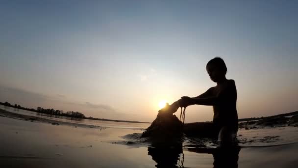 석양 모래 성을 구축 하는 해변에서 아이의 실루엣 — 비디오