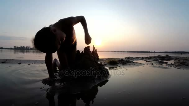 Silhouette Little Boy construye un castillo de arena al atardecer — Vídeo de stock