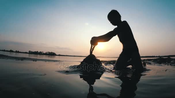 Silhouet jongetje bouwt een kasteel zand bij zonsondergang — Stockvideo