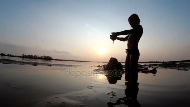 Silhouette eines Kindes am Strand, das bei Sonnenuntergang eine Sandburg baut — Stockvideo