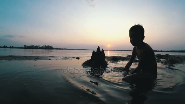 Silhouette di un bambino sulla spiaggia Costruire un castello di sabbia al tramonto — Video Stock