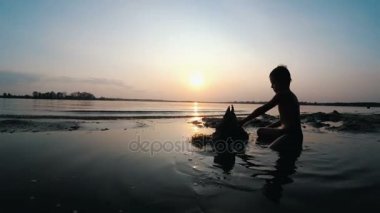 Sahilde günbatımı kum kale inşa bir çocuk silüeti