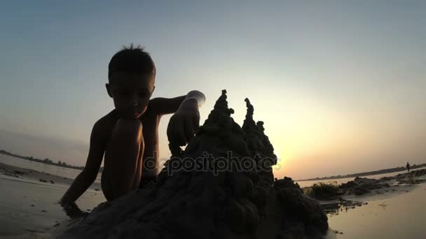 Silhouet van een kind op het strand een Sand Castle Building bij zonsondergang — Stockvideo