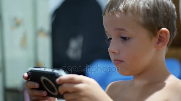 8 lat stare dziecko grając gier wideo na konsole do gier Portable, siedząc na krześle w domu — Wideo stockowe