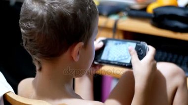 8 yaşındaki eski çocuk Video oyunları oynarken bir sandalyede evde oturan bir taşınabilir oyun konsolu üzerinde