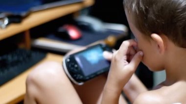 8 yaşındaki eski çocuk Video oyunları oynarken bir sandalyede evde oturan bir taşınabilir oyun konsolu üzerinde