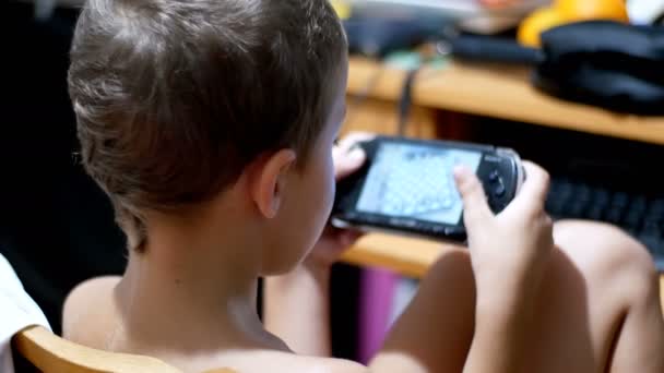 Bambino di 8 anni che gioca ai videogiochi su una console di gioco portatile seduto su una sedia a casa — Video Stock