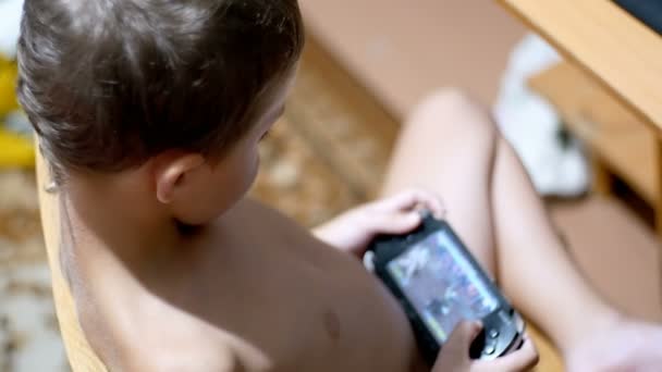 8 let starý Kid hrát videohry na přenosné herní konzole, sedí na židli doma — Stock video