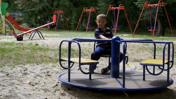 Lyckligt barn pojke Spinning på karusellen vid lekplatsen i Slow Motion — Stockvideo