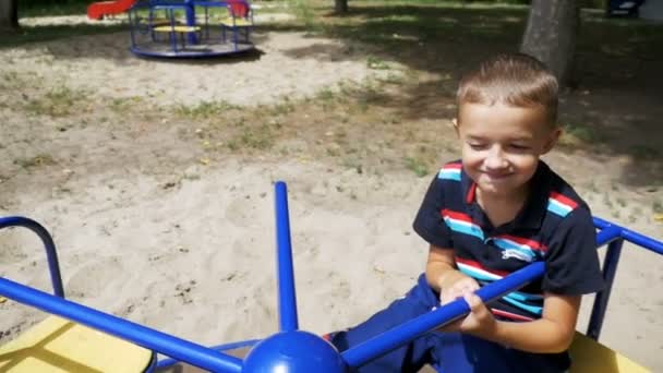 Niño feliz girando en el carrusel en el parque infantil en cámara lenta — Vídeo de stock