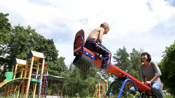 Glada barn pojke och hans mor Swinging på en Street motvikt Swing vid lekplatsen i Slow Motion — Stockvideo