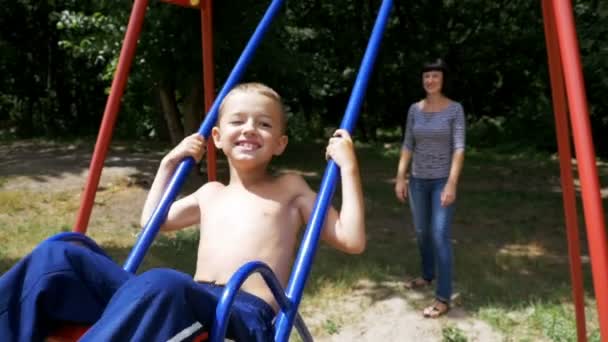 Moeder haar gelukkig kind jongen swingen op een straat schommel in speeltuin in Slow Motion — Stockvideo