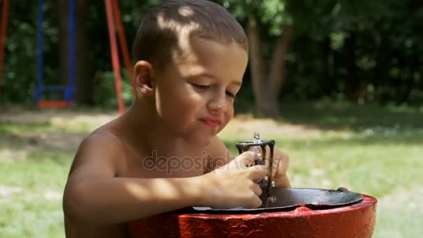 Niño feliz divertido beber agua de una fuente en el patio de recreo en cámara lenta — Vídeo de stock