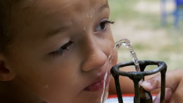 Fröhlicher kleiner Junge trinkt in Zeitlupe Wasser aus einem Trinkbrunnen auf dem Spielplatz — Stockvideo