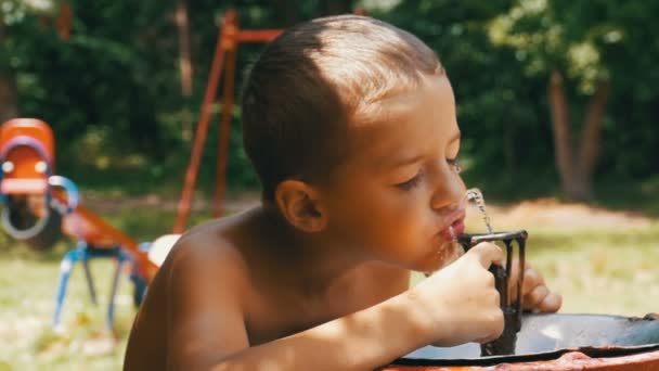 Feliz niño divertido agua potable de una fuente de agua potable en el patio de recreo en cámara lenta — Vídeo de stock