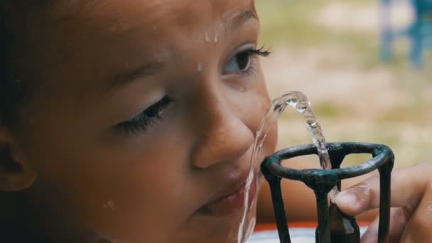 Fröhlicher kleiner Junge trinkt in Zeitlupe Wasser aus einem Trinkbrunnen auf dem Spielplatz — Stockvideo