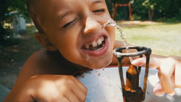 Веселый мальчик веселая питьевая вода из питьевого фонтана на детской площадке в медленном движении — стоковое видео
