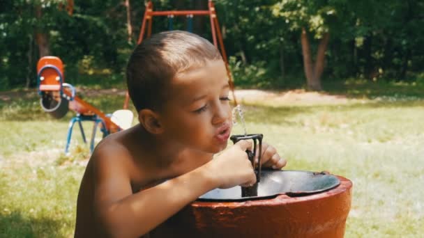 Веселый мальчик веселая питьевая вода из питьевого фонтана на детской площадке в медленном движении — стоковое видео