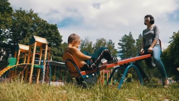 Happy Child Boy e sua mãe balançando em um balanço contrapeso de rua no playground em câmera lenta — Vídeo de Stock