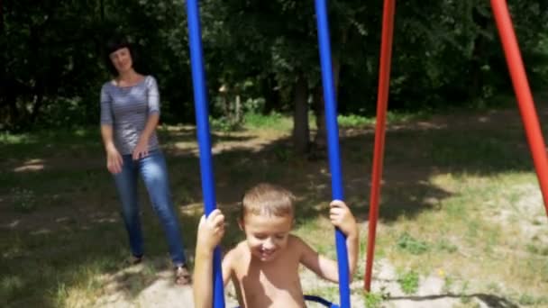 Mère balançant son enfant heureux garçon sur une balançoire de rue au terrain de jeu au ralenti — Video